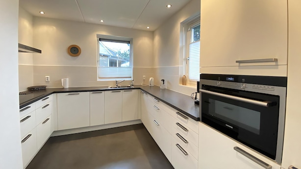 A modern kitchen with white cabinets, a black countertop, and a built-in oven.