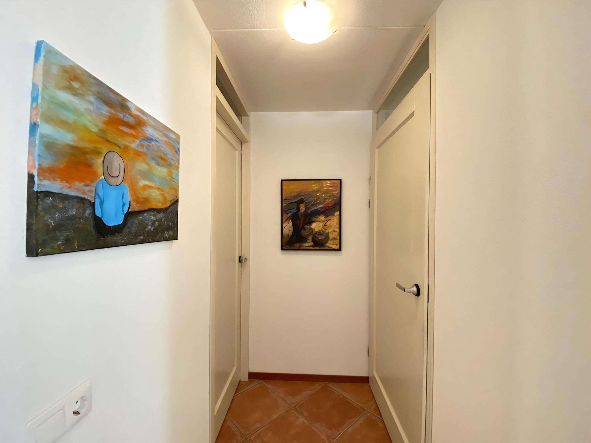 Un pasillo con dos puertas, un cuadro en la pared izquierda e iluminación en el techo.