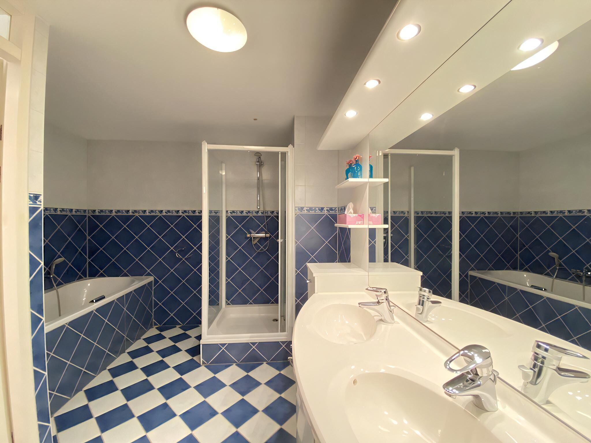 Casa de banho com chão quadriculado azul e branco, lavatório branco, espelho e cabine de duche.
