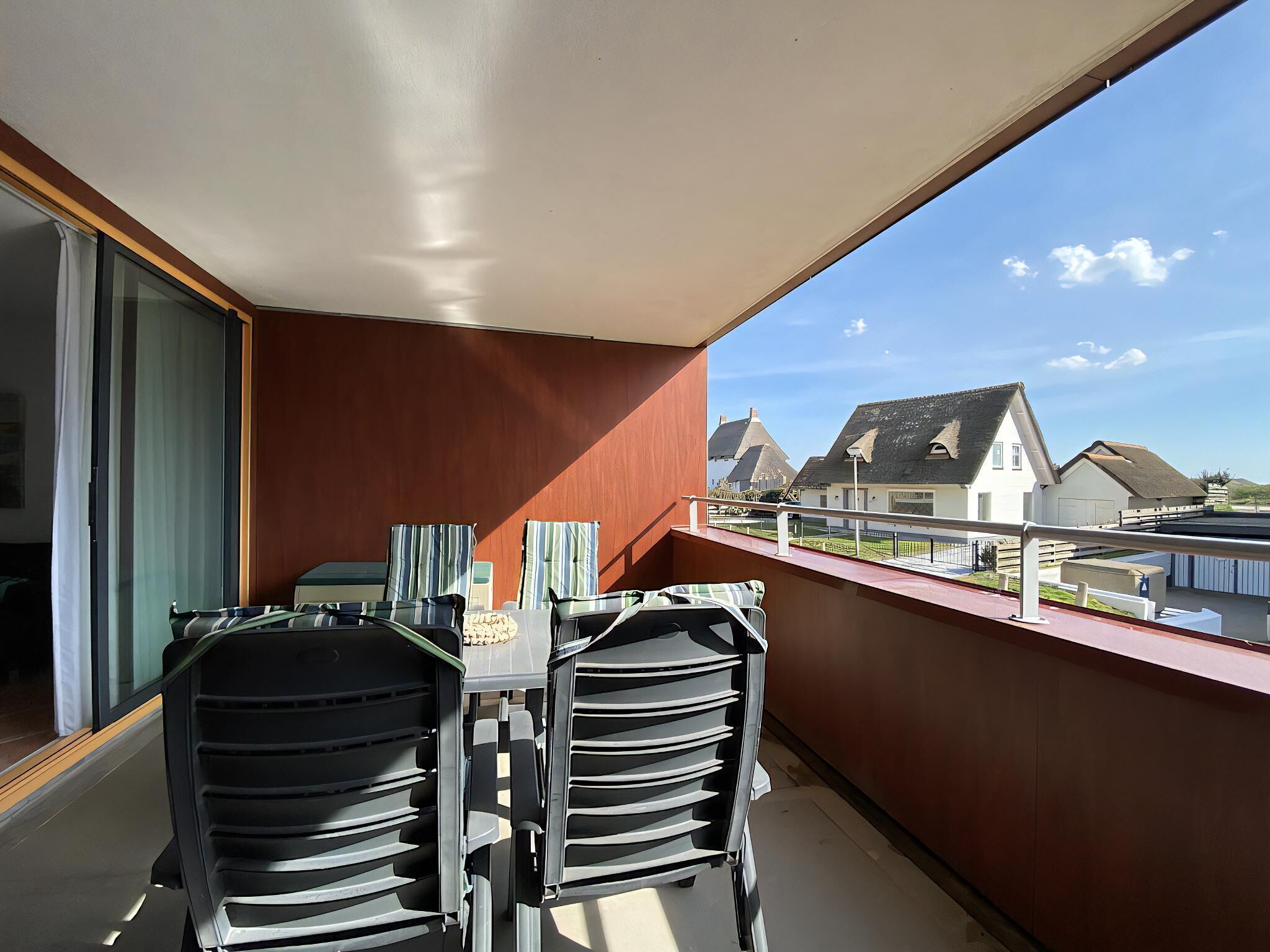 A balcony with a table and chairs, a view of houses, and a clear sky.