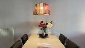 Una zona pranzo con tavolo, sedie, un vaso con fiori e una lampada a sospensione.