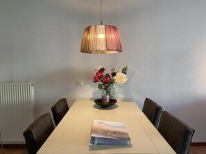 A dining area with a table, chairs, a vase with flowers, and a hanging lamp.