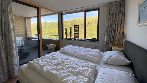 Una camera da letto con un letto grande, una finestra vista su un paesaggio verde e un balcone con una sedia e un tavolo.