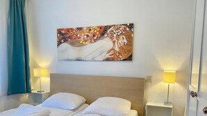 A hotel room with a double bed, two bedside tables with lamps, a wall-mounted artwork, and a door with a handle.