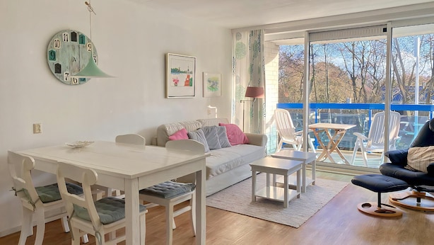 A modern living room with a dining area, a sofa, and a balcony with outdoor seating.