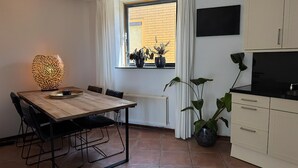 Cocina compacta con comedor, que incluye un ventanal con plantas en macetas, una lámpara moderna y un televisor de pantalla plana.