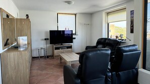 Un salon avec un téléviseur, un meuble en bois, une table basse et un canapé en cuir noir.