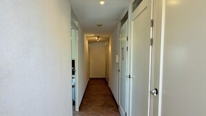 Un couloir étroit aux murs blancs et au sol carrelé, qui mène à une porte sur laquelle se trouvent un téléphone et une pancarte.