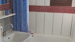 A bathroom with a white sink, a mirror, a window, and a red-tiled shower area.