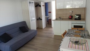 A compact living space with a sofa, a dining table with cookies, a kitchen area with a kettle, and a walk-in closet.