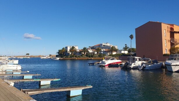 A marina with boats docked, a clear sky, and buildings in the background.