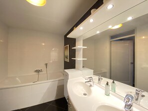 A modern bathroom with a bathtub, a large mirror, and a vanity with a sink and multiple faucets. - Callantsoger Staete A402 (Callantsoog)