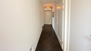 En smal hall med mörkt kakelgolv och vita väggar.
