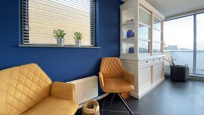 Ett modernt vardagsrum med en blå vägg, en gul soffa, en trästol och ett vitt skåp med hyllor.