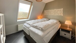 Ett sovrum med en stor säng, ett takfönster, en dekorativ väggpanel och ett nattduksbord med en lampa.