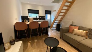 Un espace de vie moderne comprenant une cuisine, un coin repas avec quatre chaises, un canapé et un escalier.