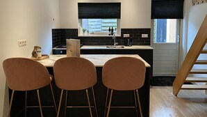 Une cuisine moderne avec un îlot central, un dosseret de carreaux noirs et trois chaises marron.