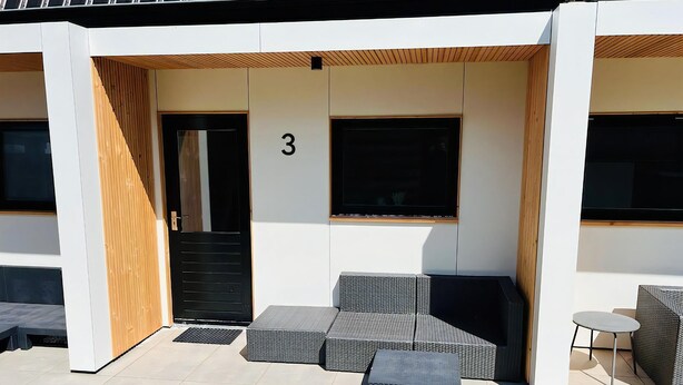 Un bâtiment moderne avec le chiffre « 3 » affiché sur le mur, un espace extérieur aménagé avec des meubles en osier et de grandes fenêtres.