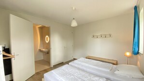 A hotel room with two beds, a bathroom with a sink, a mirror, and a coat rack.