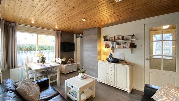 A cozy living room with a wooden ceiling, a sofa, a coffee table, a TV, and a bookshelf. - 2 bedroom accommodation in Callantsoog (Callantsoog)