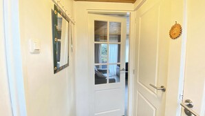 A narrow hallway with a white door at the end, a small window, and a wooden ceiling. - 2 bedroom accommodation in Callantsoog (Callantsoog)