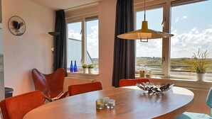 A modern dining area with a wooden table, orange chairs, and a view of the countryside through large windows. - 3 bedroom accommodation in Callantsoog (Callantsoog)