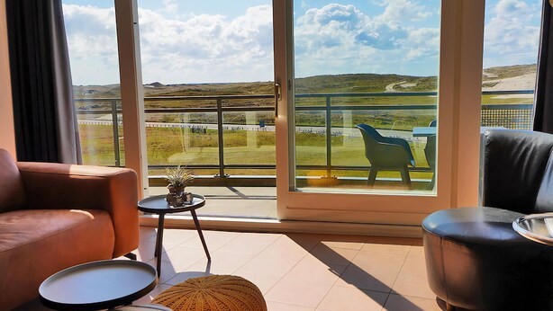 A modern living room with a large window offering a view of a golf course and distant hills. - 3 bedroom accommodation in Callantsoog (Callantsoog)