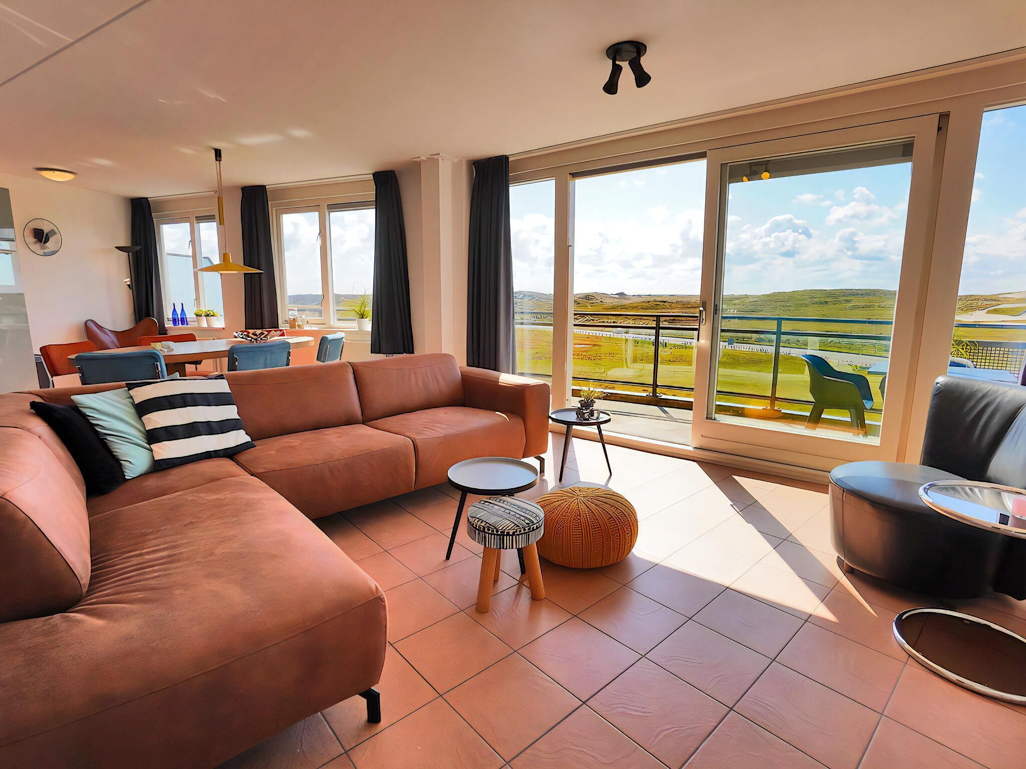 A spacious living area with a large sofa, a small round table, and a view of a green landscape through large windows.