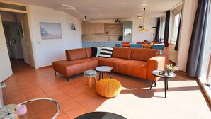 A modern living room with a sectional sofa, a small round table, and a dining area in the background. - 3 bedroom accommodation in Callantsoog (Callantsoog)