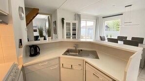 A modern kitchen with white cabinetry, a built-in dishwasher, and a large window providing natural light. - 2 bedroom accommodation in Callantsoog (Callantsoog)