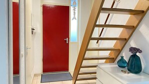 A modern interior with a red door, a wooden ladder, and a white console table with decorative vases. - 2 bedroom accommodation in Callantsoog (Callantsoog)