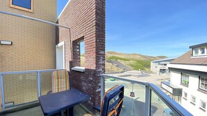 Ein Balkon mit Tisch und gestreiftem Stuhl, mit Blick auf einen Parkplatz und Gebäude.