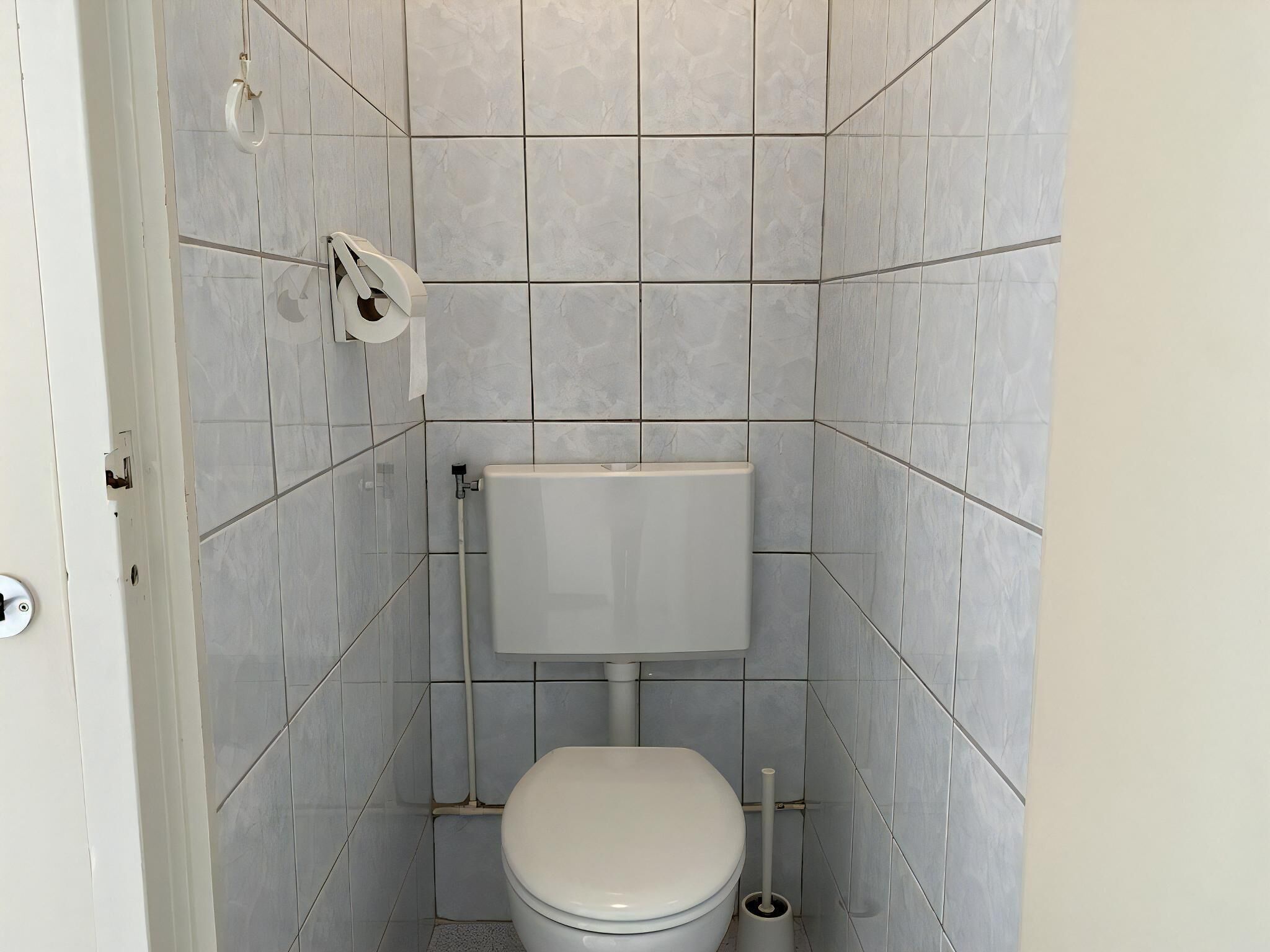 Une petite salle de bain compacte comprenant des toilettes, un porte-rouleau de papier toilette et un bidet.
