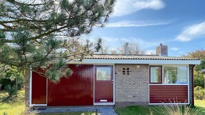 A modern single-story house with a red garage, a brick wall, and a metal roof. - 2 bedroom accommodation in Callantsoog (Callantsoog)