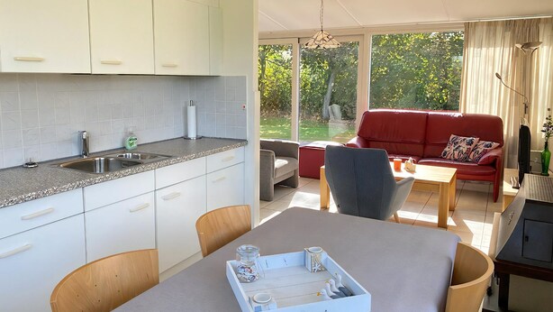 A modern kitchen with a built-in sink and a dining area with a table and chairs. - 2 bedroom accommodation in Callantsoog (Callantsoog)