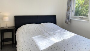 A bedroom with a bed, a bedside table, a lamp, and a window with curtains. - 2 bedroom accommodation in Callantsoog (Callantsoog)