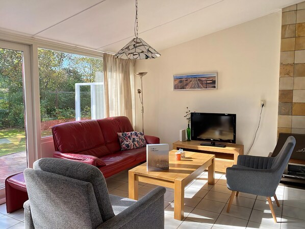 A modern living room with a red sofa, grey armchairs, a wooden coffee table, and a flat-screen TV.