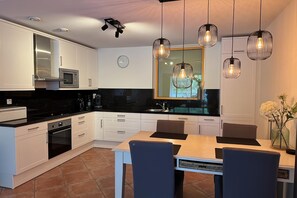 A modern kitchen with white cabinets, a black countertop, a built-in microwave, and a dining area with a table and chairs. - Callantsoger Staete A03 (Callantsoog)