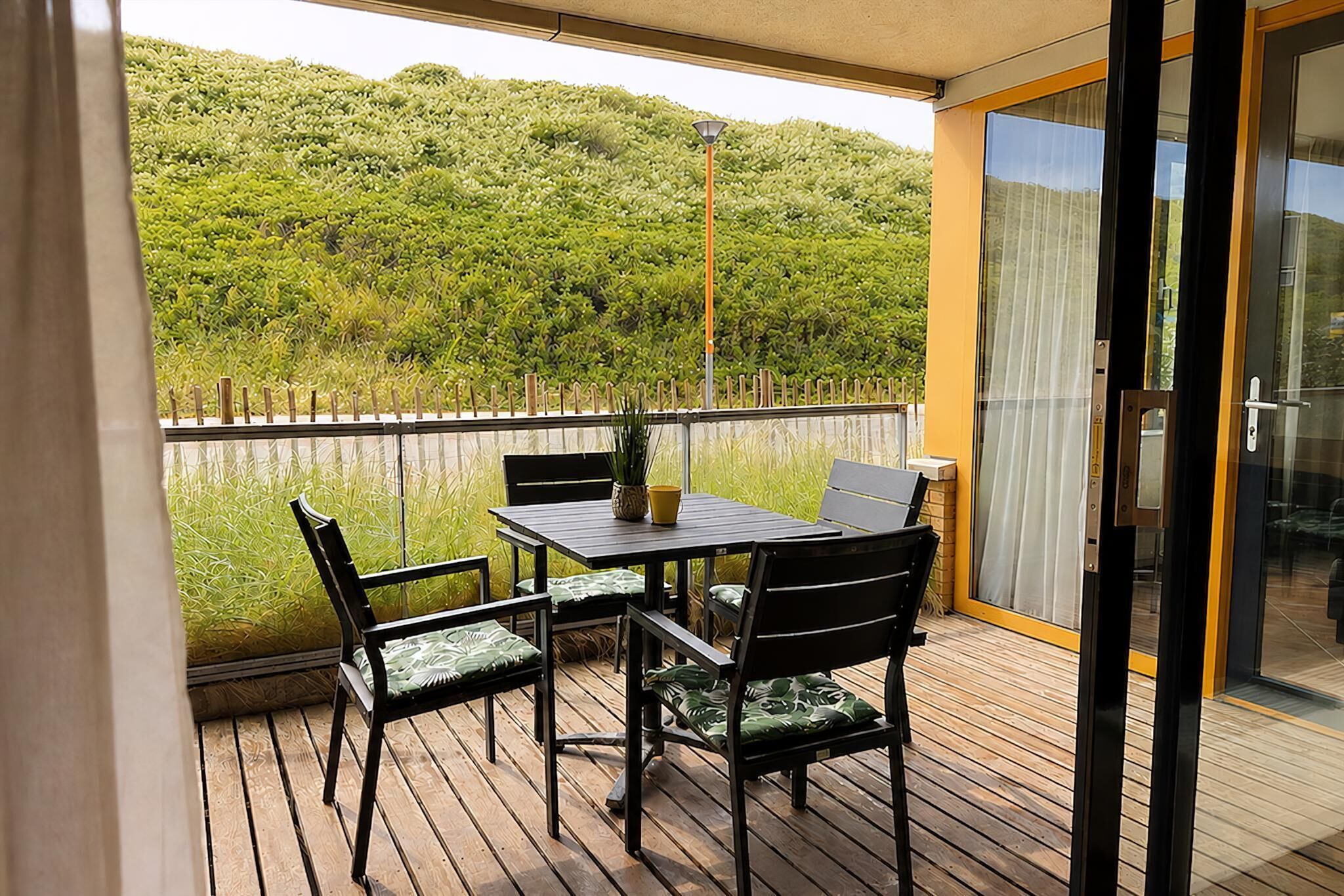 Een balkon met een tafel en stoelen, een uitzicht op een groene heuvel en een glazen deur.