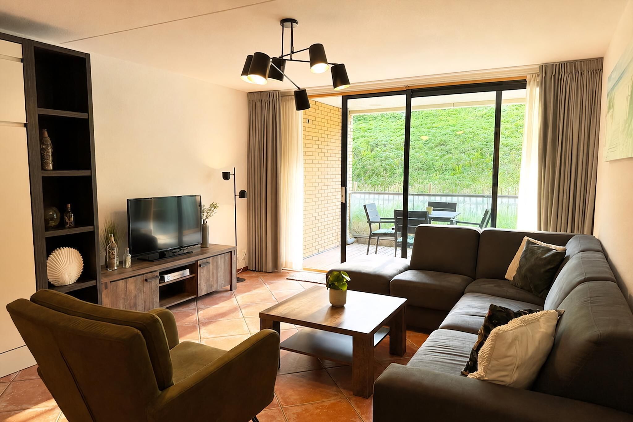 A living room with a sofa, a coffee table, a TV, a bookshelf, and a sliding glass door leading to a balcony.