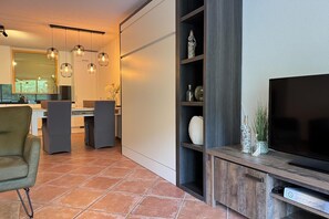 Un salon moderne doté d’un téléviseur à écran plat, d’un meuble de rangement en bois et d’un coin repas avec une grande fenêtre.