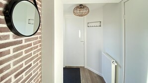 Een gang met een bakstenen muur, een ronde spiegel, een witte deur, een plafondlamp en een radiator.