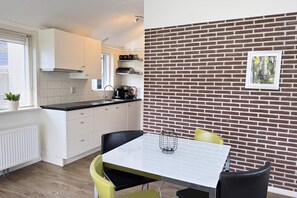 A modern kitchen with white cabinets, a black countertop, and a brick wall with a framed picture. - 2 bedroom accommodation in Callantsoog (Callantsoog)