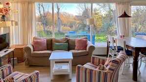 A cozy living room with a sofa, striped armchairs, a small table, and a view of the garden through large windows. - 3 bedroom accommodation in Callantsoog (Callantsoog)