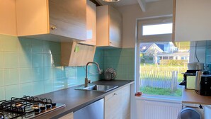 A modern kitchen with a gas stove, stainless steel sink, and a window with a view of a residential area. - 3 bedroom accommodation in Callantsoog (Callantsoog)