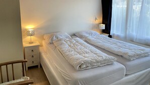 A twin room with two beds, a nightstand, a wooden chair, and a window with curtains. - 3 bedroom accommodation in Callantsoog (Callantsoog)