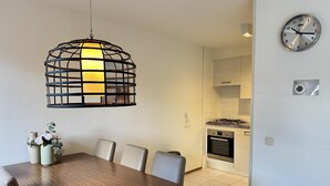 Ett modernt matområde med ett träbord och stolar, en hängande lampa och utsikt över ett kök med en spis och ugn.
