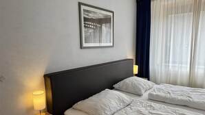 A hotel room with a bed, a nightstand with a lamp, a framed picture on the wall, and a window with curtains. - Callantsoger Staete A08 (Callantsoog)