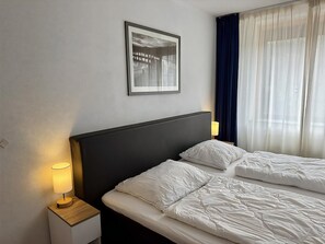 A hotel room with a bed, a nightstand with a lamp, a framed picture on the wall, and a window with curtains. - Callantsoger Staete A08 (Callantsoog)