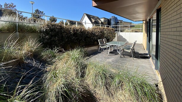 An outdoor patio with a table and chairs, a covered area, and a view of a residential building. - Callantsoger Staete A08 (Callantsoog)